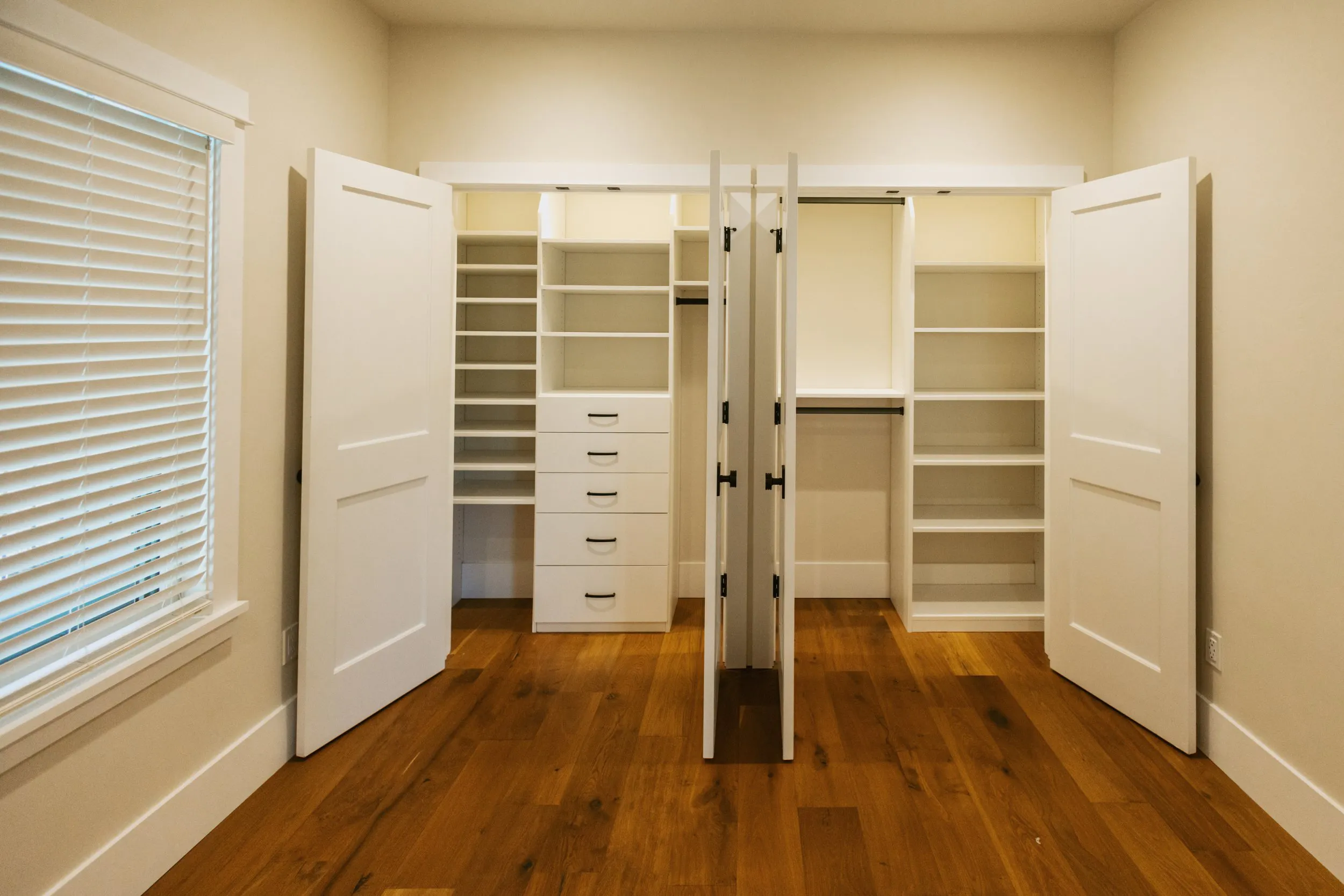 A spacious, well-organized white closet with multiple shelves and drawers, featuring wooden floors and white doors, designed by Devengenzo & Company in Lafayette.