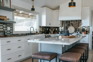 A modern kitchen featuring white cabinets, a large marble island with brown stools, hexagonal backsplash tiles, and contemporary light fixtures by Diablo Valley Cabinetry in San Ramon.