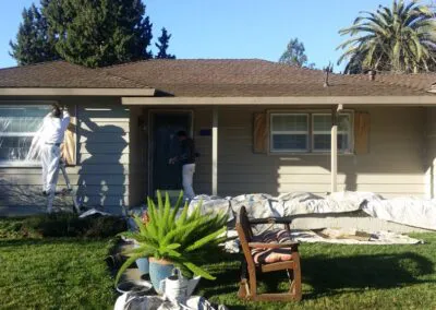 Two workers from DiazandSonsConstruction painting the exterior of a house in Santa Rosa, with tools and materials set up in the yard.