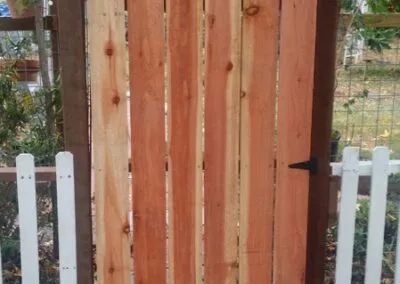 A wooden gate with vertical planks, accompanied by a white picket fence, crafted by DiazandSonsConstruction in SantaRosa.