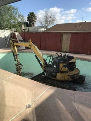 A construction excavator working inside an empty swimming pool, part of a renovation project.