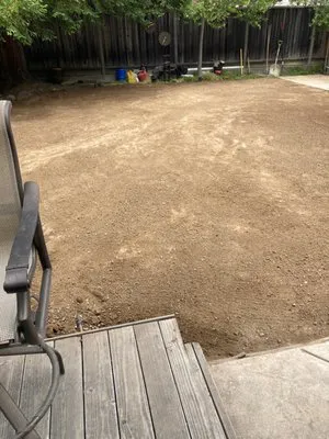 A leveled dirt backyard in San Ramon, prepared for landscaping by Dig & Demo, featuring a wooden deck and garden tools in the background.