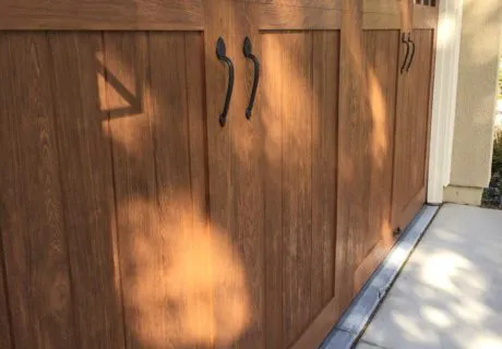 A wooden garage door with detailed craftsmanship and elegant hardware, installed by Door Pros, Inc. in San Rafael, casting shadows on the ground.