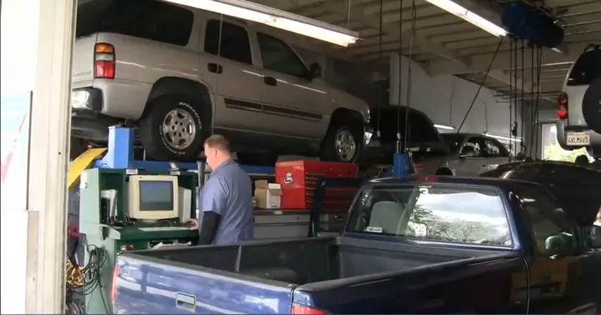 A mechanic in a shirt stands at a diagnostic machine inside a garage, with multiple vehicles elevated on lifts in the background at Dublin Car Tek in Dublin.