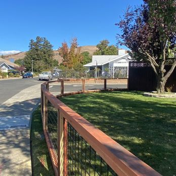 A newly constructed wooden and wire fence enclosing a well-maintained lawn in a residential neighborhood under a clear blue sky, built by Duce Construction, Inc. in Walnut Creek.