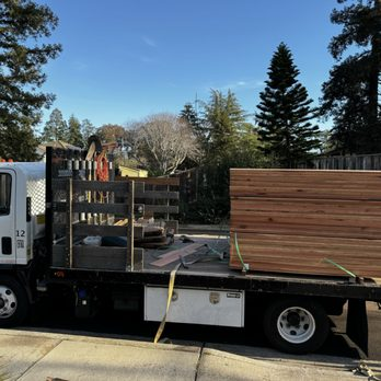 A truck loaded with wooden planks from Duce Construction, Inc. parked on a street in Walnut Creek, surrounded by trees.