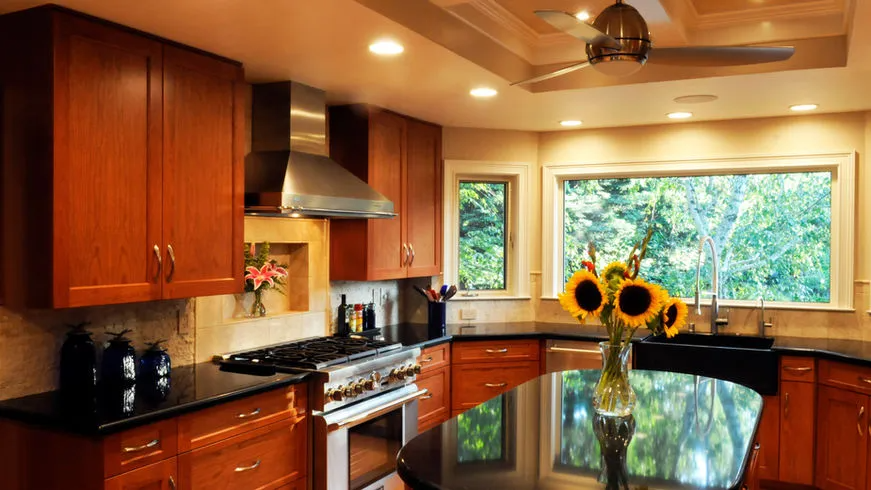 A modern kitchen with wooden cabinets and a sleek black countertop, featuring sunflower decor and large windows overlooking greenery, designed by Dutcher Construction in Sacramento.