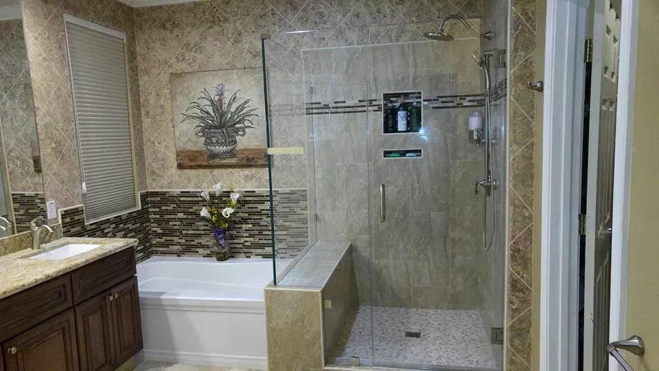 A modern bathroom with a glass shower enclosure and bathtub, featuring a tiled design and a vanity with a marble countertop. Created by East Bay PC Construction, Inc. in Brentwood.
