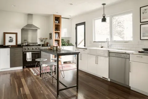 A modern kitchen in Brentwood with white cabinets, a stainless steel stove, a large sink, and a central island table with stools, designed by East Bay PC Construction, Inc.