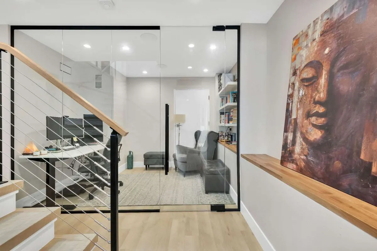 A modern interior in Walnut Creek featuring glass-walled office space by Edri Construction, with a large Buddha painting on the wall and a minimalistic staircase.