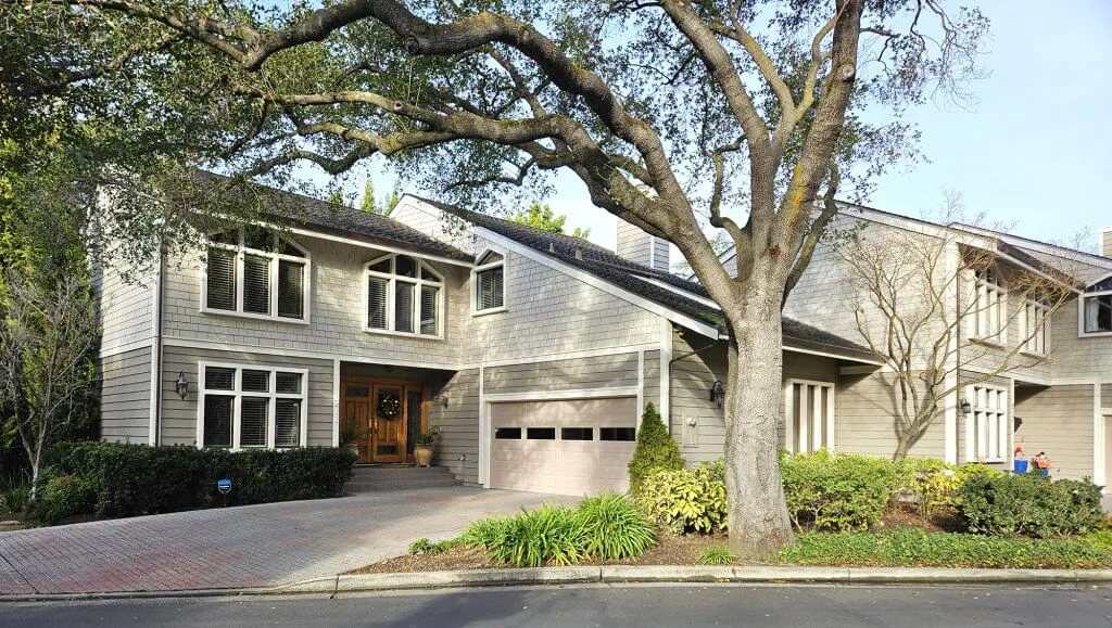 Exterior view of a renovated, two-story house with a gray facade, surrounded by greenery, showcasing work by El Gato Painting & Restoration, Inc. in Mountain View.