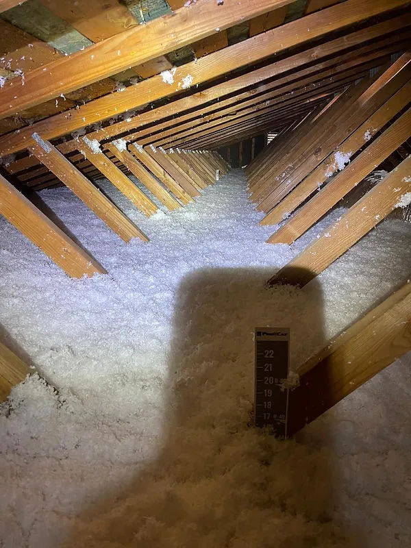 An attic space with wooden beams and thick insulation material on the floor, illuminated by a flashlight, showcasing Electro-Integrity's work in San Francisco.