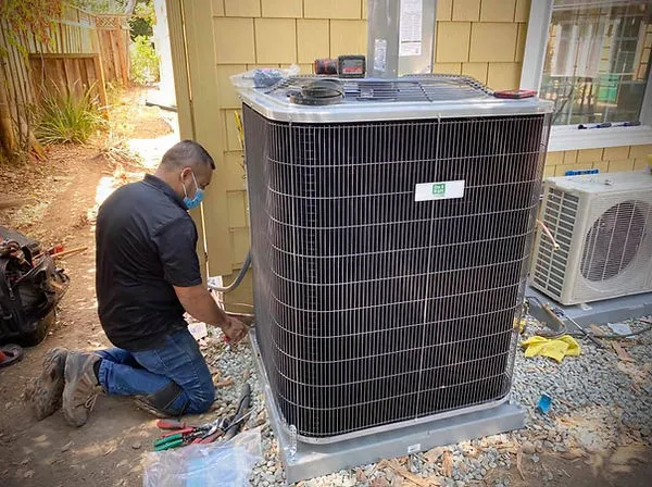 Technician kneeling and working on an HVAC unit outside a house, surrounded by tools and equipment.