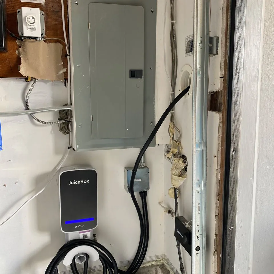 An electrical setup in a garage featuring a JuiceBox electric vehicle charger, circuit breaker panel, and electrical wiring.