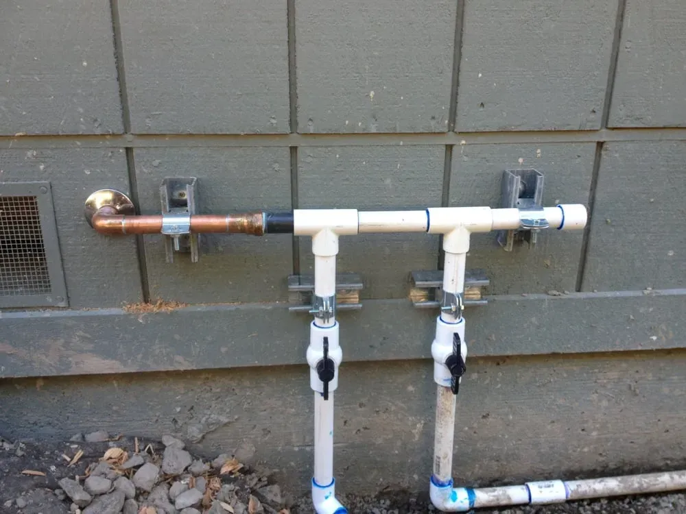 Outdoor piping system with copper and PVC pipes installed on the exterior wall of a building, demonstrating precise plumbing work by ElitePlumbingServices in Cotati.
