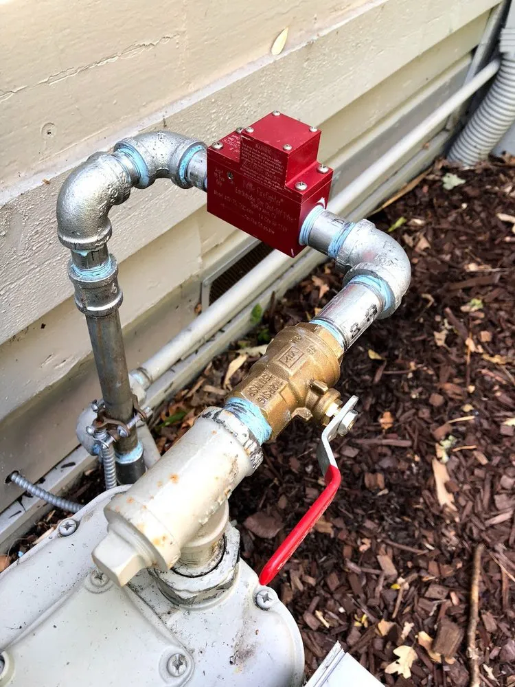 Close-up of a red valve and gas pipe system installed outdoors, surrounded by mulch, illustrating plumbing work by ElitePlumbingServices in Cotati.