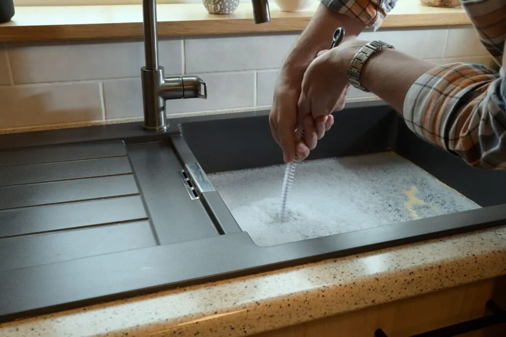 A person using a brush to clean a sink filled with soapy water, highlighting effective plumbing practices by ElitePlumbingServices in Cotati.