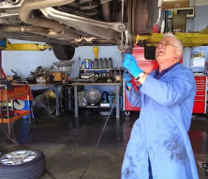 A mechanic in a blue coat working on a car lifted in a garage at European Sales & Service, Santa Rosa.