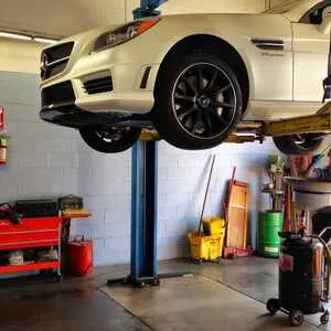 A white car on a lift inside a garage, surrounded by various tools and equipment, representing the auto service environment at European Sales & Service in Santa Rosa.