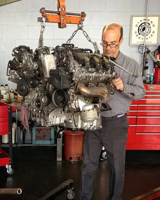 A mechanic at European Sales & Service in Santa Rosa carefully inspects a car engine suspended in a workshop.