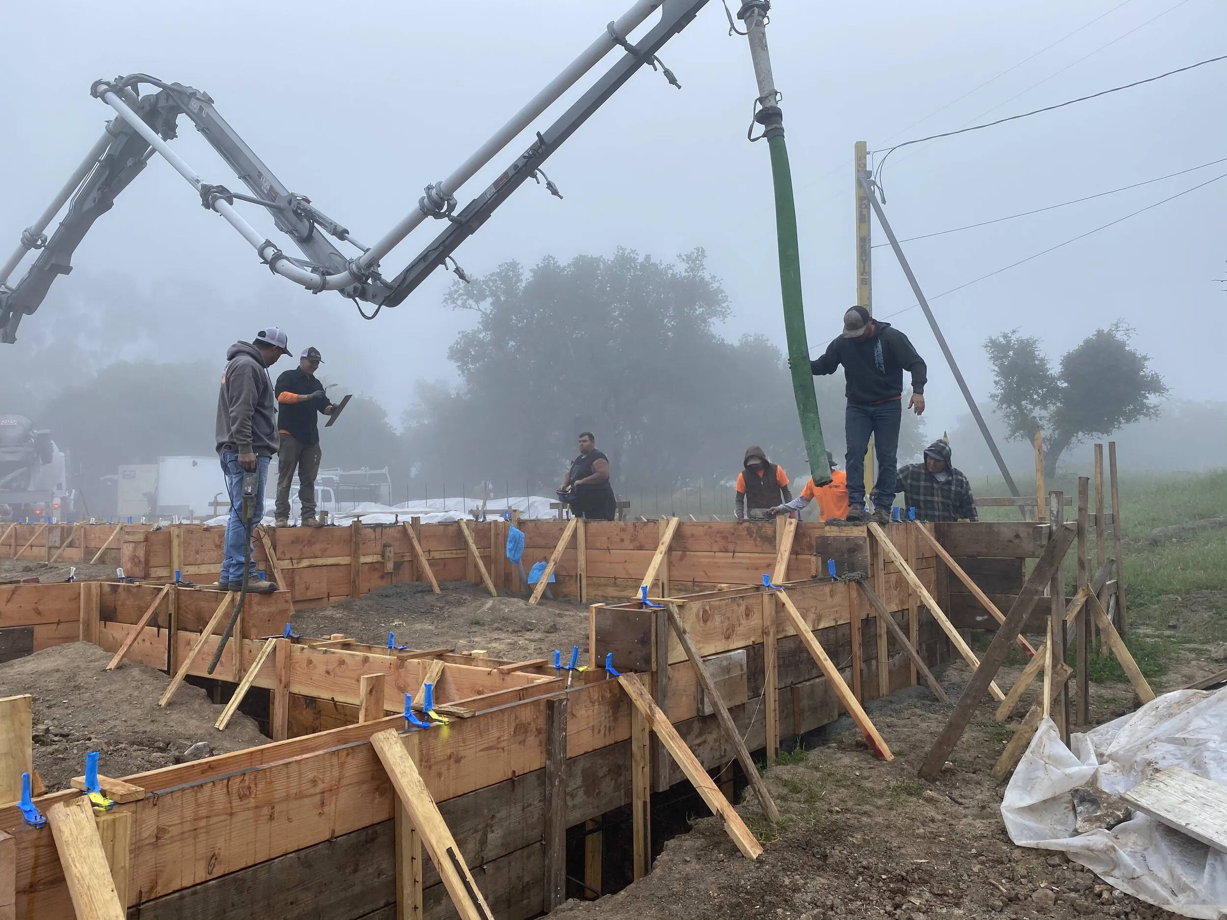 Construction workers with concrete machinery pouring concrete into wooden frameworks on a foggy day at a construction site in Petaluma.