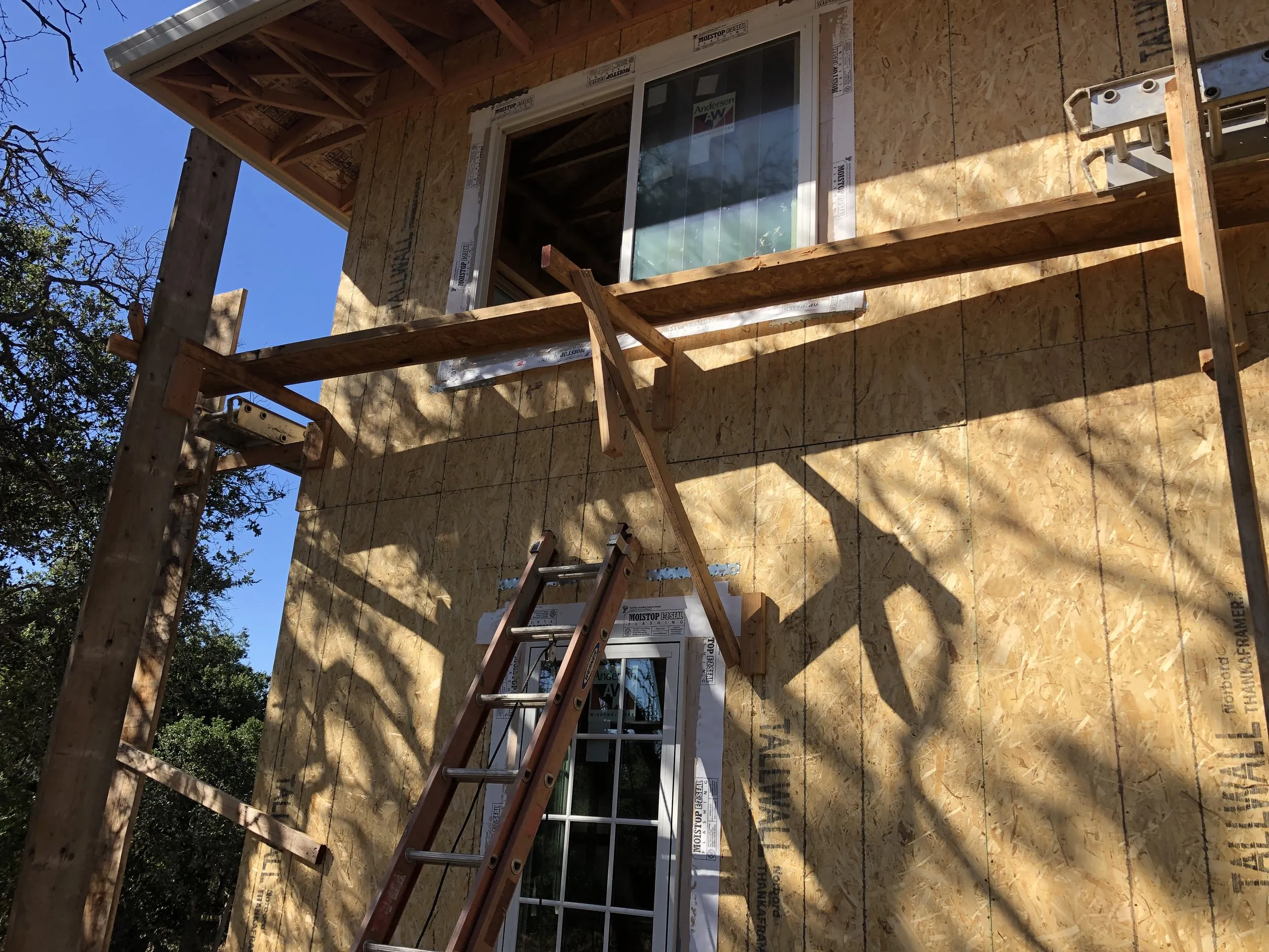 "Construction site showing a wooden structure with a ladder leaning against it under a clear blue sky."
