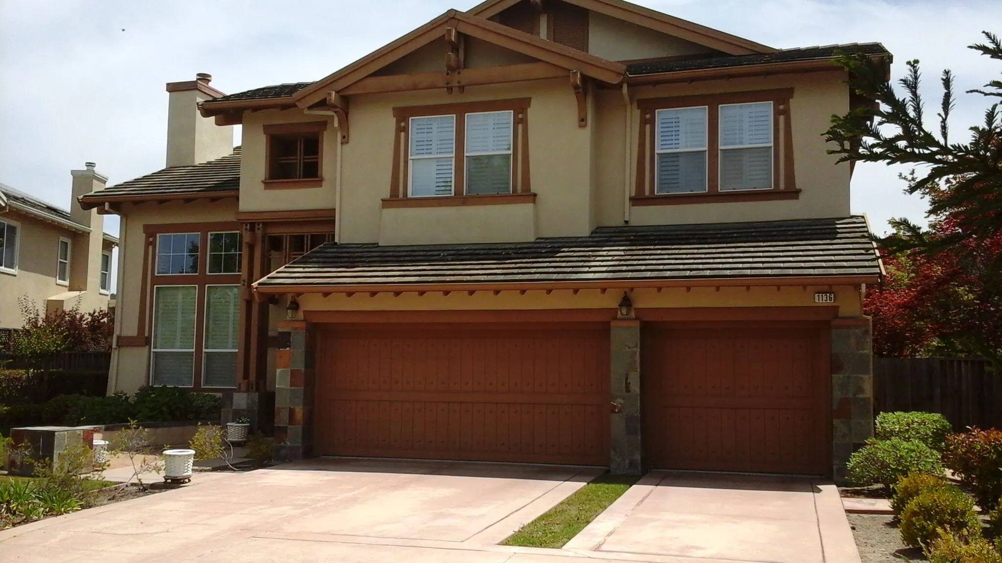 A well-maintained two-story house with beige and brown paintwork, featuring double garages and surrounded by a neat garden, showcasing the workmanship of FaithPainting in San Jose.