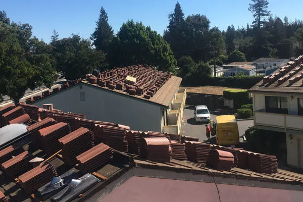 A view of rooftops undergoing renovation with stacks of red tiles, taken in a residential area in SanJose, with trees and a delivery truck visible in the background.