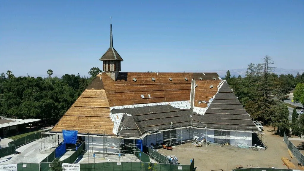 A wooden-roofed building undergoing restoration by FalconRoofing in San Jose, with scaffolding and construction materials visible.