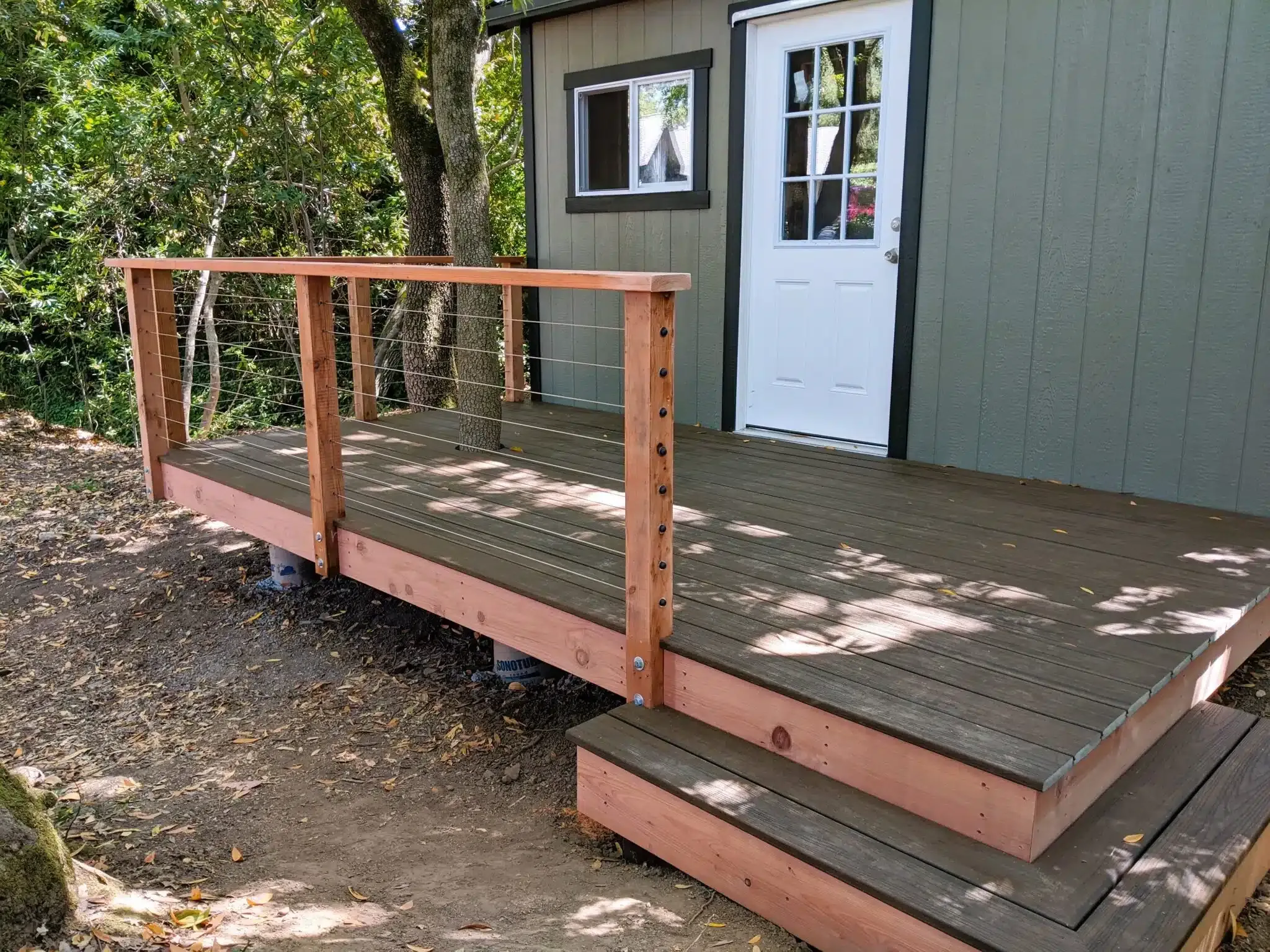 A wooden deck with cable railing, constructed by Farrar Construction Inc., attached to a small building, surrounded by trees in Petaluma.