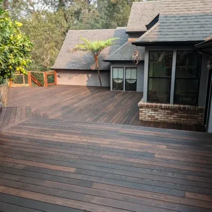 A spacious wooden deck designed by Farrar Construction Inc. in Petaluma, featuring detailed woodwork and surrounded by lush greenery and a modern house.