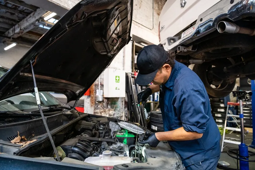 A mechanic at Faxon Garage in San Francisco works under the hood of a car, focused on engine maintenance.