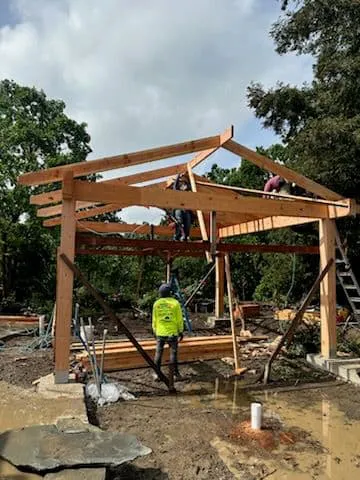Workers from Fernandez & Sons Landscaping Inc. constructing a wooden frame structure outdoors in Concord, with trees and building materials visible in the background.