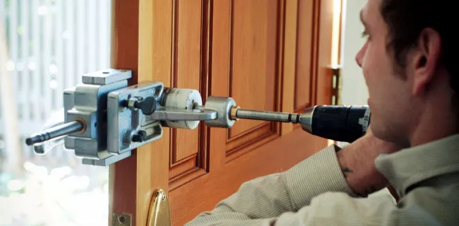 A person using a drill to install a lock in a wooden door, demonstrating the lock installation process by First Lock & Security Technologies.