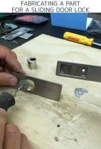 Close-up image of a person using a tool to fabricate a part for a sliding door lock on a workbench with lock components.