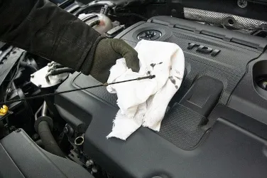 A person wearing gloves checks the oil level on a dipstick over a car engine, emphasizing attention to detail and maintenance at Fremont Foreign Auto in Fremont.