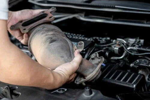 A person holding a catalytic converter in an engine bay at Fremont Foreign Auto in Fremont.