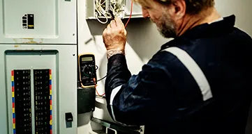 An electrician from Frontline Electrical Services working on a circuit breaker panel with a multimeter in Benicia.