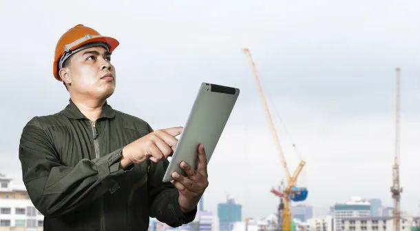 An engineer in a hard hat using a tablet on a construction site, representing Frontline Electrical Services in Benicia.