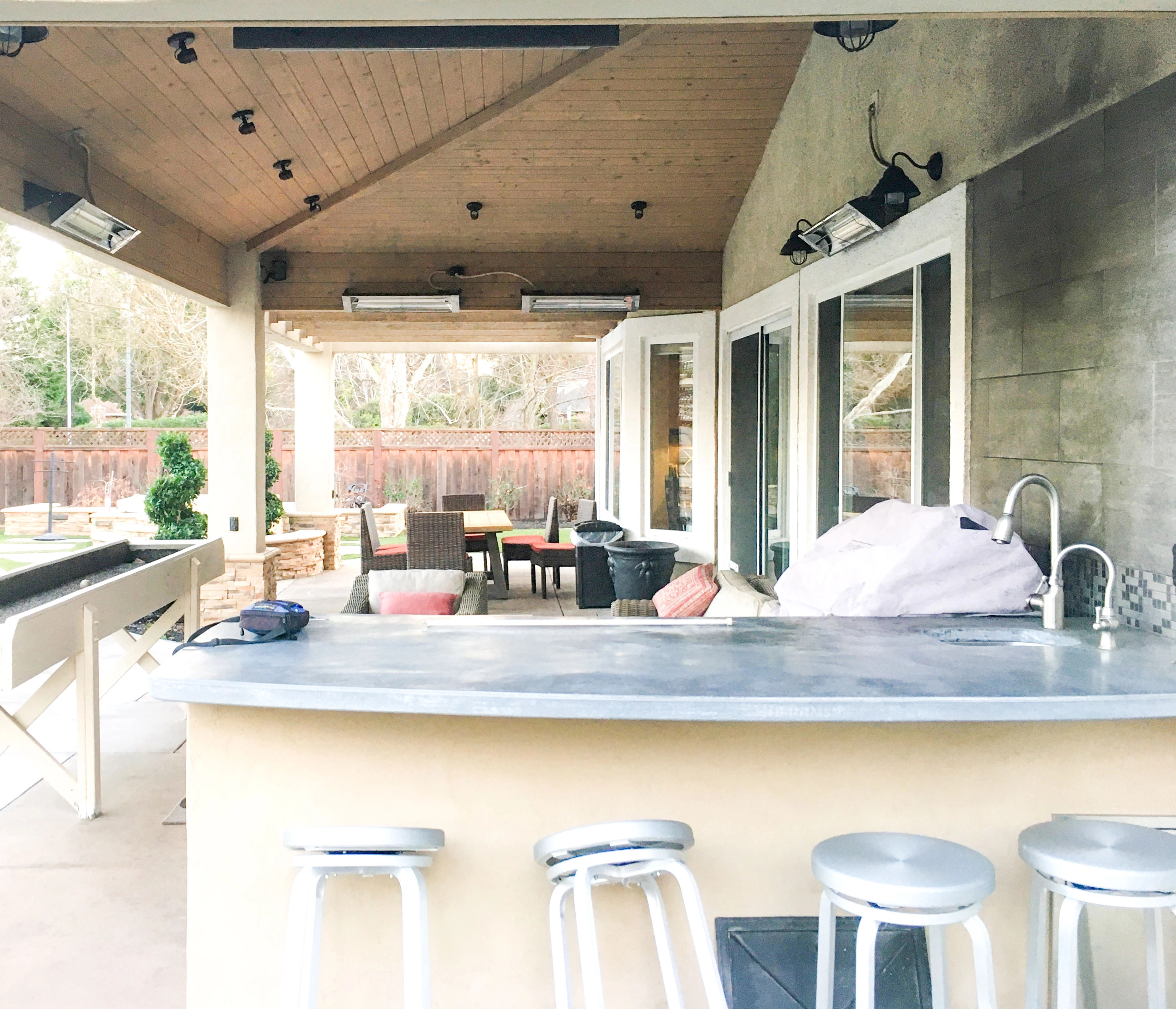 An outdoor patio with a countertop and bar stools, designed by GK Construction in Pleasanton, featuring a shaded seating area with tables and patio furniture.