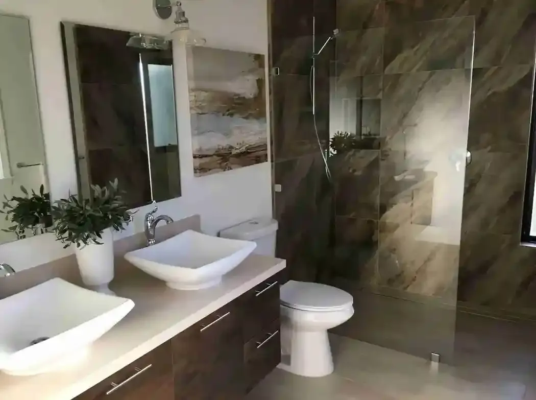 A modern bathroom featuring dual square sinks, a glass-enclosed shower, a toilet, and contemporary decor, designed by G. D. Enterprise in Redwood City.