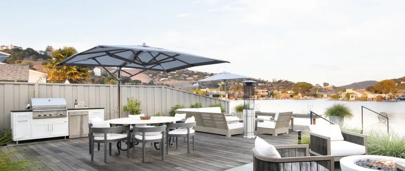 Outdoor patio featuring modern furniture, a grill, large umbrellas, and a scenic water view, designed by G Landscape Division, LLC in San Rafael.