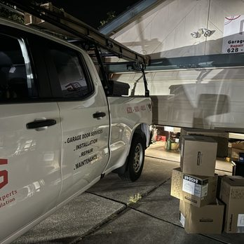 "A service truck from Garage Door Experts Repair & Installation, LLC parked in front of a partially open garage door, with tools and boxes nearby, depicting a repair scene in Fremont."