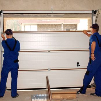 Two technicians in blue uniforms installing a garage door in a residential setting.