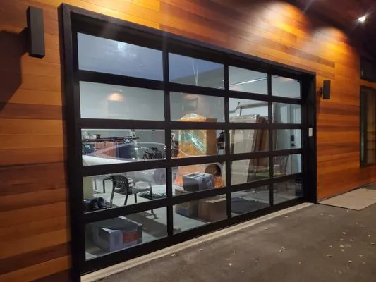 A modern garage door with transparent panels, installed in a wooden facade, showcasing the interior of a garage with various items, by Garage Door Pros in Sunnyvale.