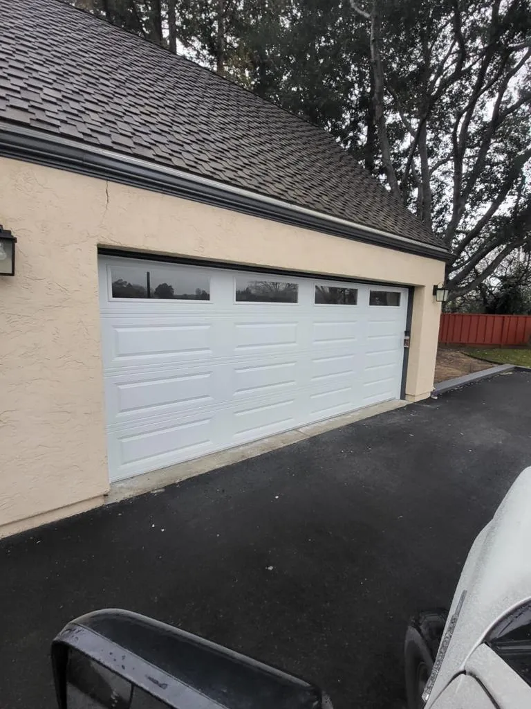 "A white garage door installed on a beige building, surrounded by a driveway and trees, by Garage Door Pros in Sunnyvale."