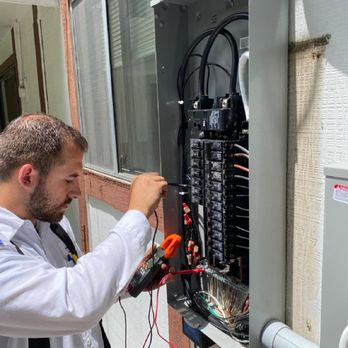 A technician in a white shirt works with tools on an open electrical panel, demonstrating professional maintenance by Genesis Electric in Vallejo.
