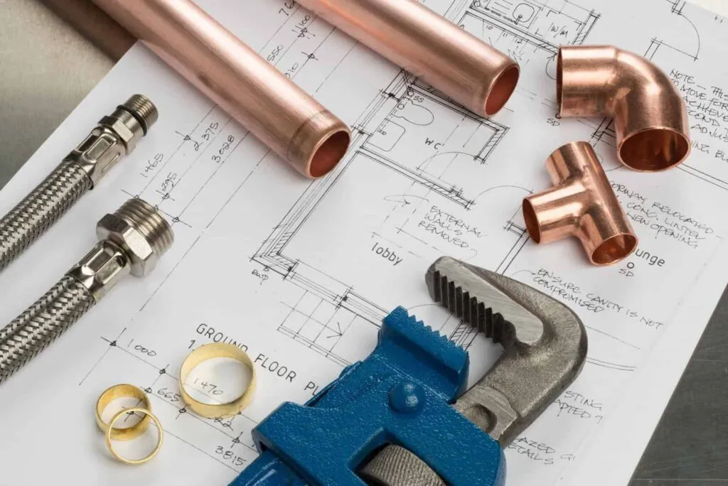 "Plumbing tools including pipes, fittings, a wrench, and a blueprint on a workbench, used by Gogo Rooter in San Jose."