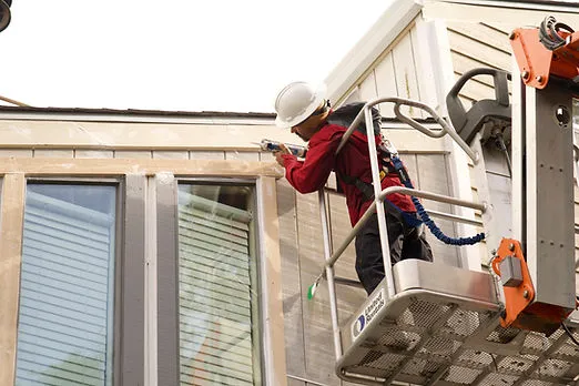 A worker in a cherry picker wearing a hard hat, performing maintenance on the exterior of a building.