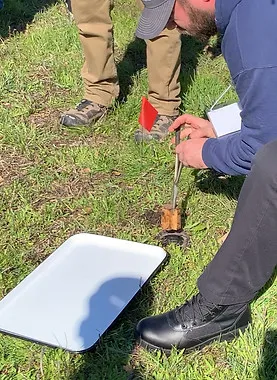 A person in outdoor clothing inspecting the ground with tools, next to a white tray and red flag, representing Great Wall Termite Control's thorough inspection process in San Jose.